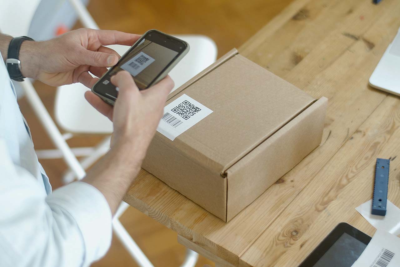 Image of a person using their phone to scan a QR code on a cardboard package.